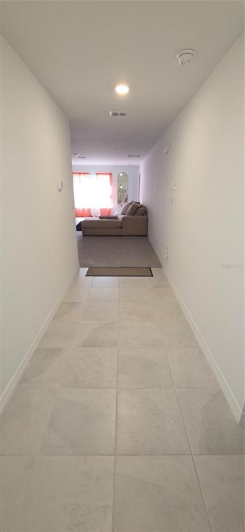 A tiled hallway leads into a carpeted living room with a sofa and orange curtains — 558 TASCO AVENUE SW, PALM BAY, FL