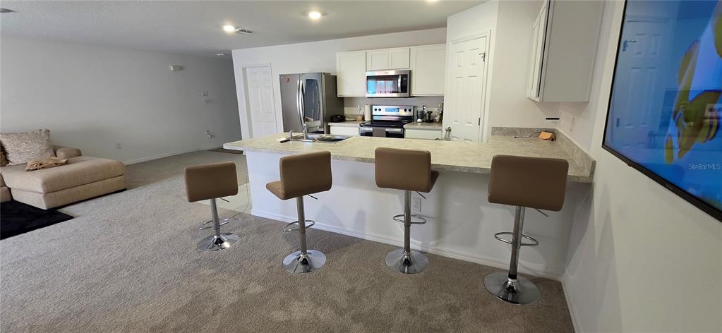 A kitchen with a breakfast bar and four stools opens into a carpeted living area — 558 TASCO AVENUE SW, PALM BAY, FL