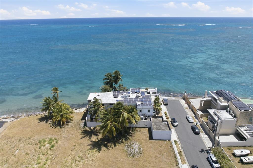 An aerial view shows a coastal house with solar panels next to a paved street — 4 EMAJAGUA, SAN JUAN, PR