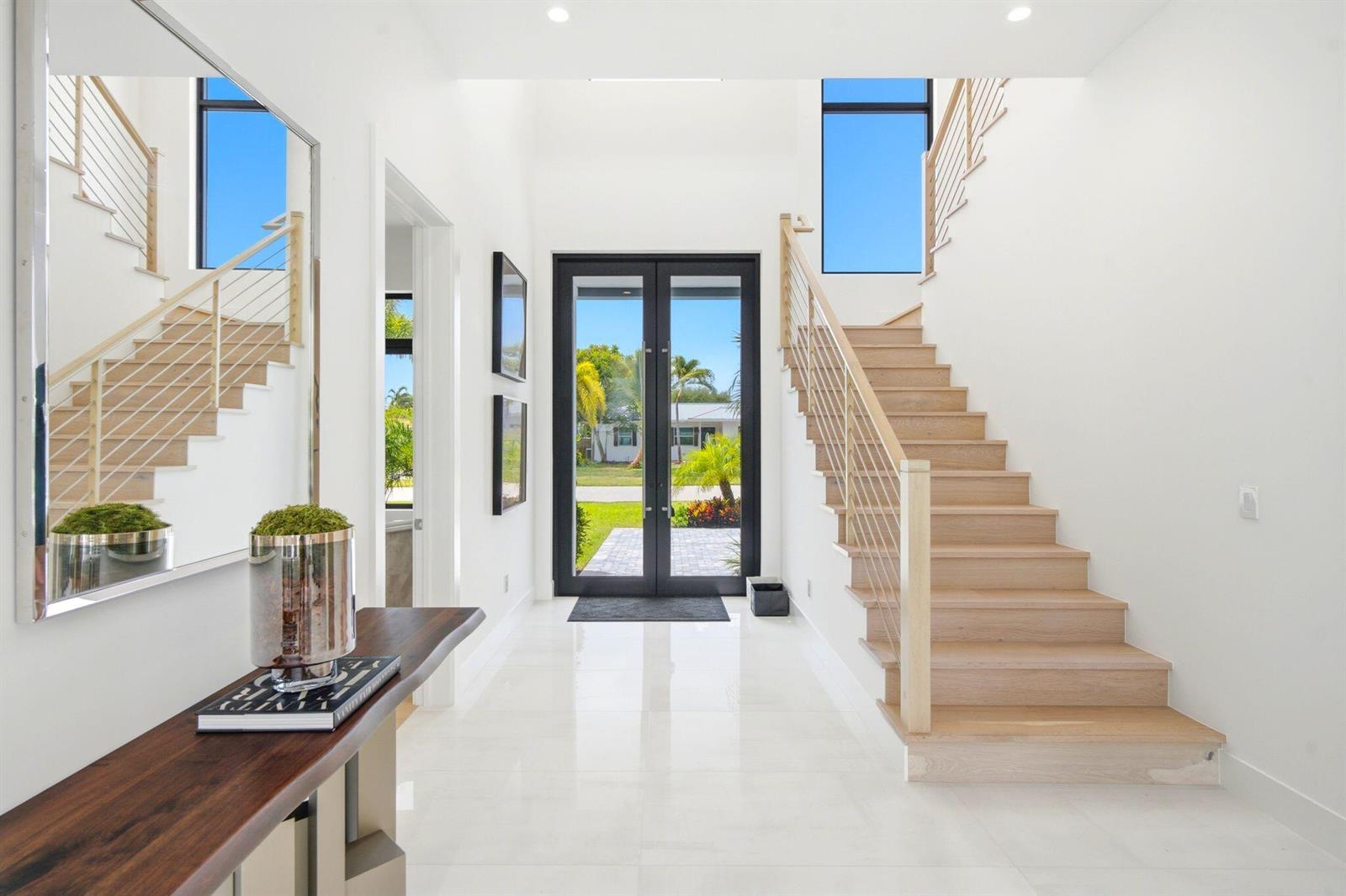 A bright entryway features white tile floors, a wooden staircase with cable railings, and double doors — 261 NW 8th Street, Boca Raton FL 33432, BOCA RATON, FL