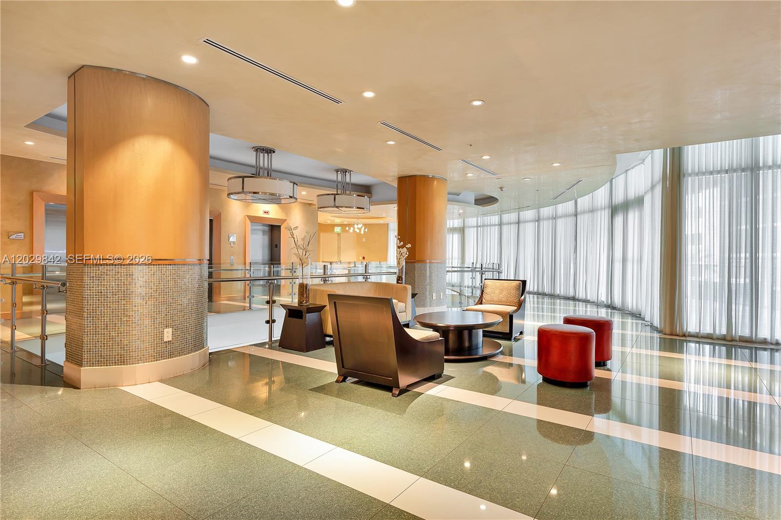 A modern lobby features curved wooden columns, tile flooring, and floor-to-ceiling windows with curtains — 218 SE 14th St, Miami FL 33131, MIAMI, FL