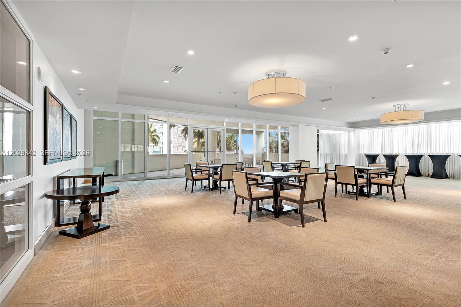 A spacious, carpeted event room features multiple dining tables, large windows, and modern light fixtures — 218 SE 14th St, Miami FL 33131, MIAMI, FL