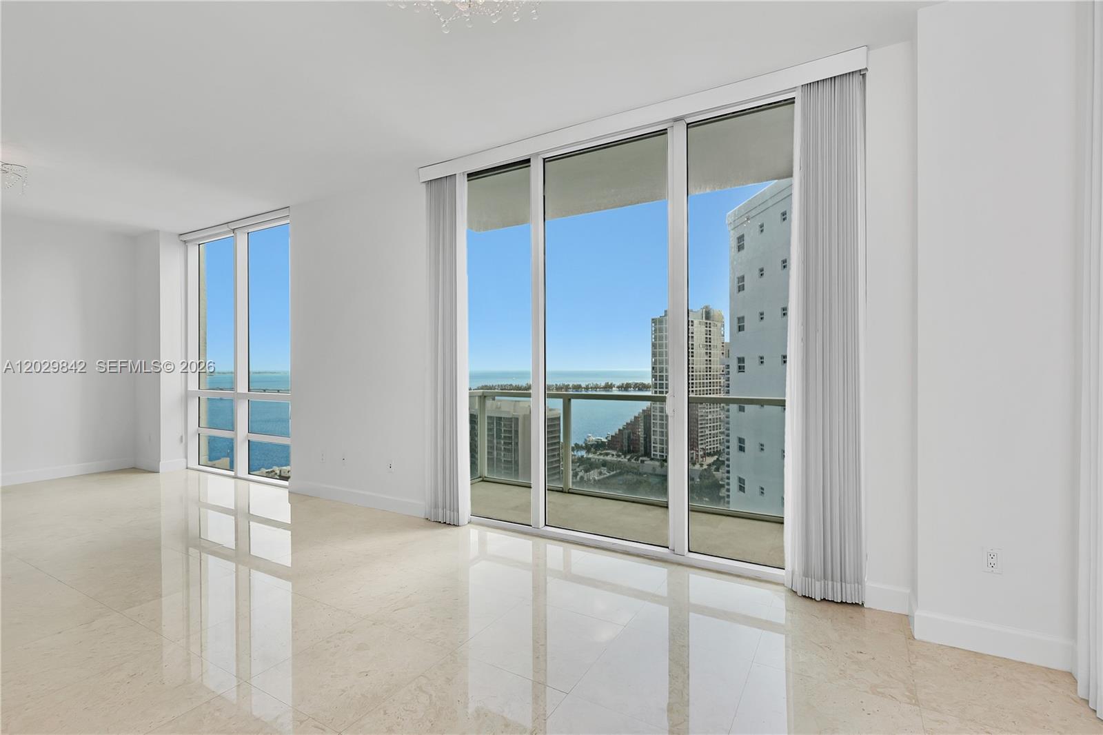 An empty room with white walls, polished tile floors, and large windows overlooking the ocean — 218 SE 14th St, Miami FL 33131, MIAMI, FL