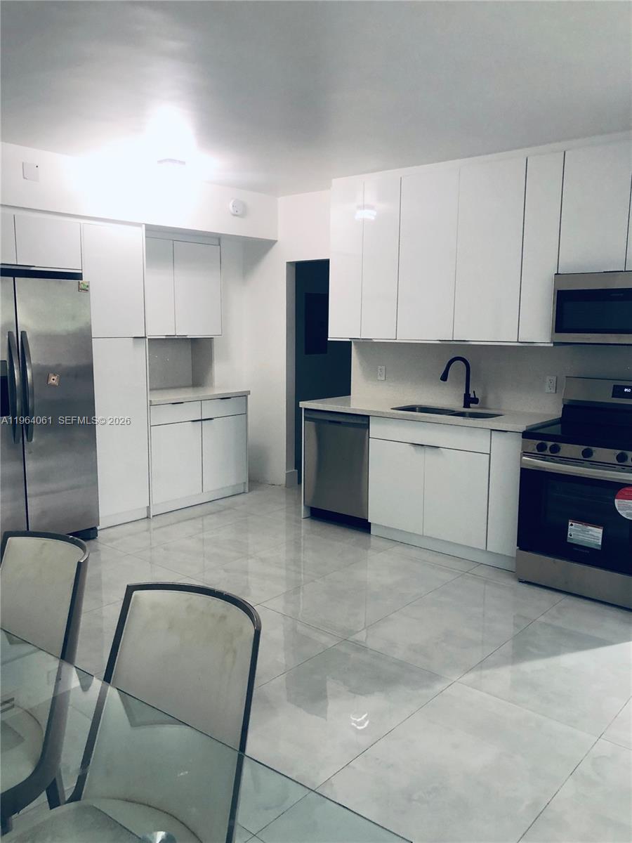 A modern kitchen features white cabinets, stainless steel appliances, and light-colored tile flooring — 10185 Collins Ave # 209, Bal Harbour FL 33154, BAL HARBOUR, FL
