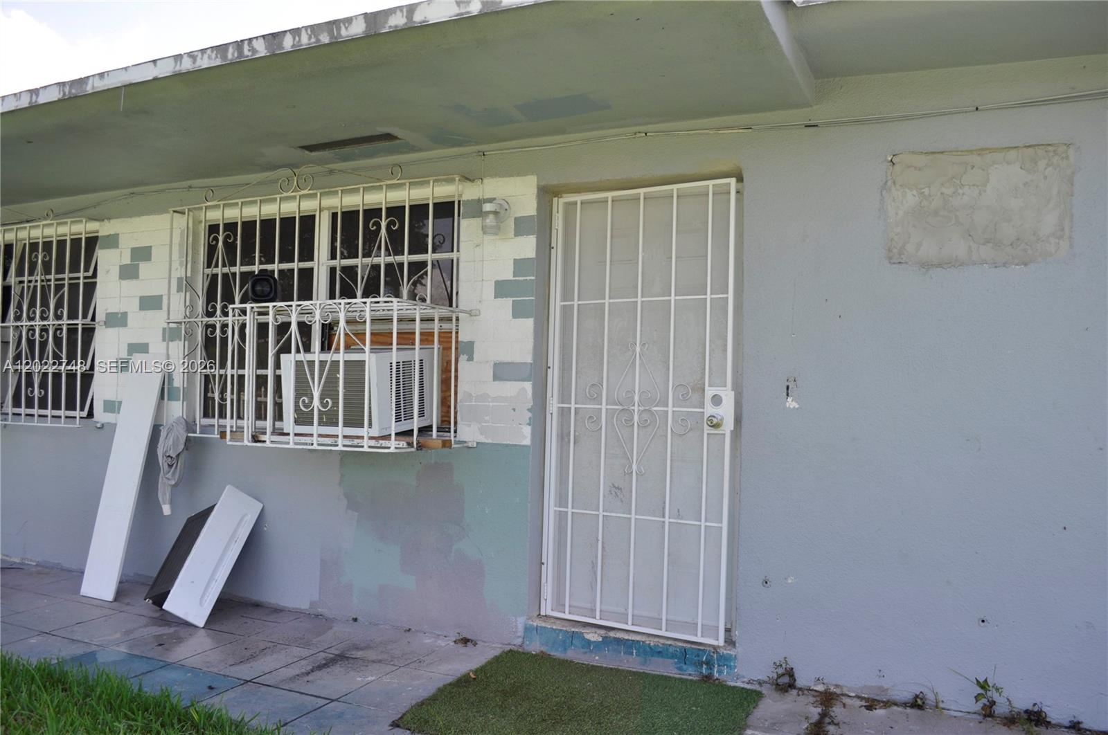 The exterior of a building shows a door with a security gate and a window unit — 2395 NW 82nd St # 2395, Miami FL 33147, MIAMI, FL