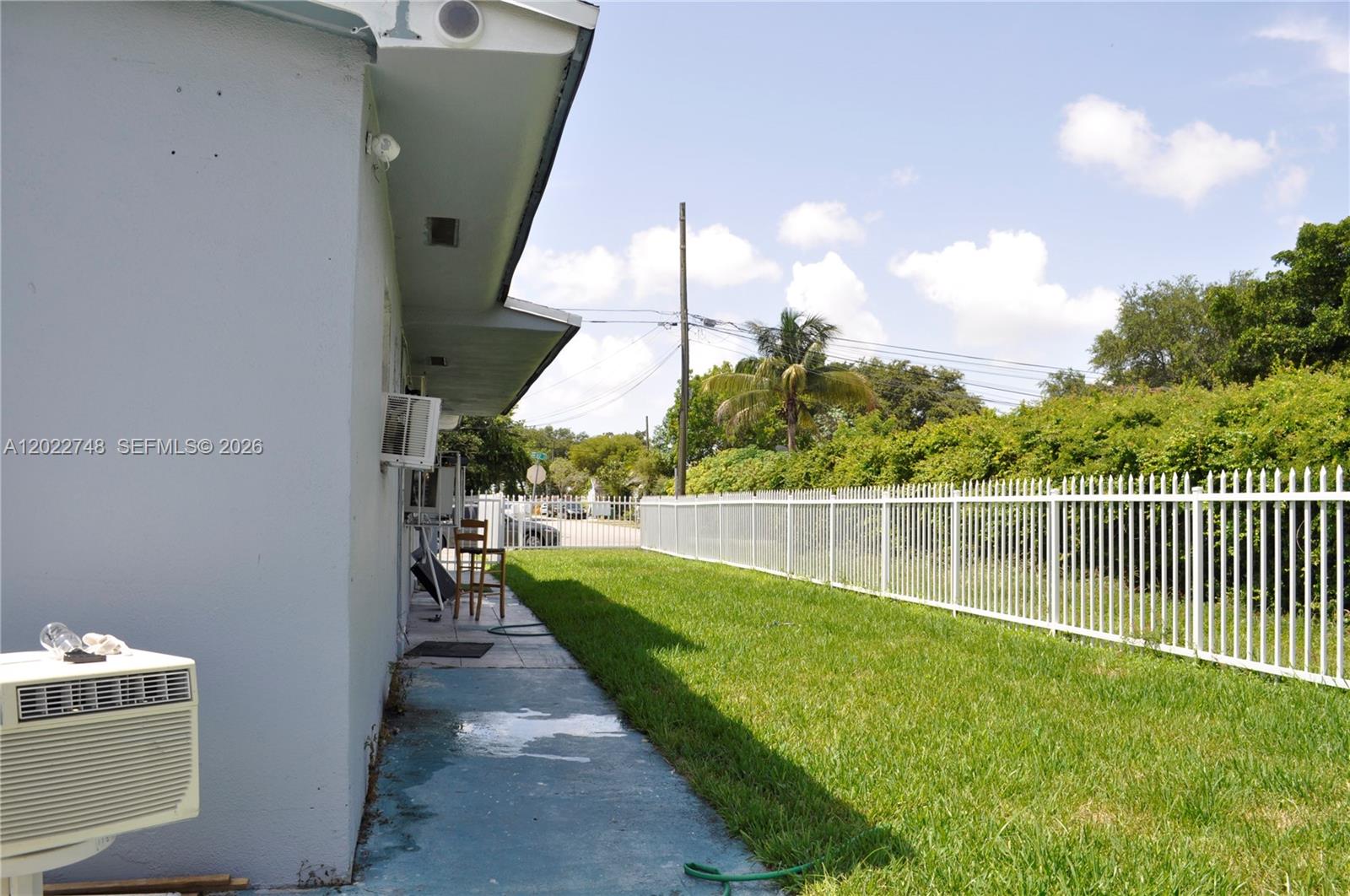 A side view of a house exterior shows a concrete walkway, lawn, and white fence — 2395 NW 82nd St # 2395, Miami FL 33147, MIAMI, FL
