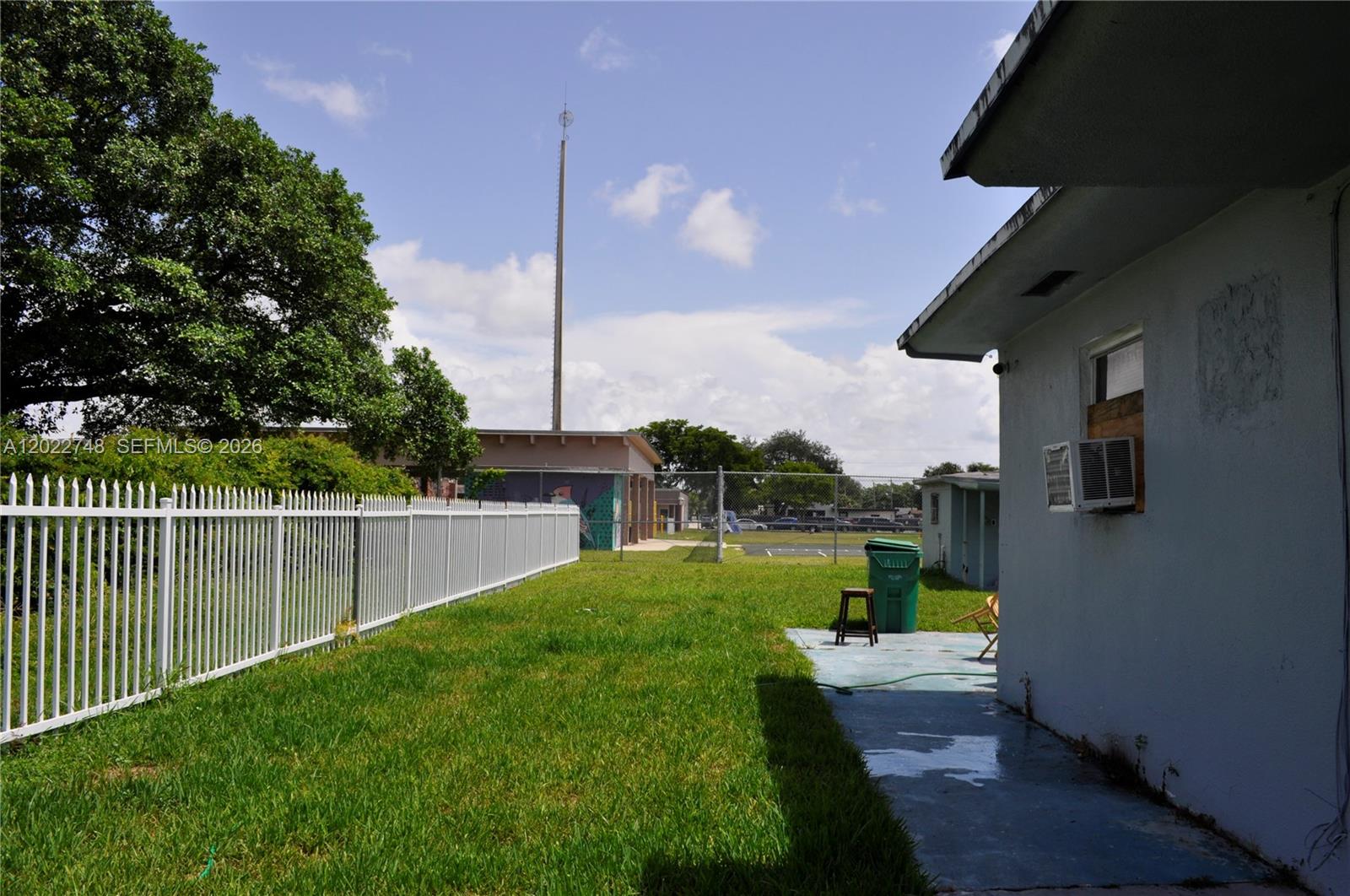 A grassy backyard features a white fence, a concrete patio, and a green trash bin — 2395 NW 82nd St # 2395, Miami FL 33147, MIAMI, FL