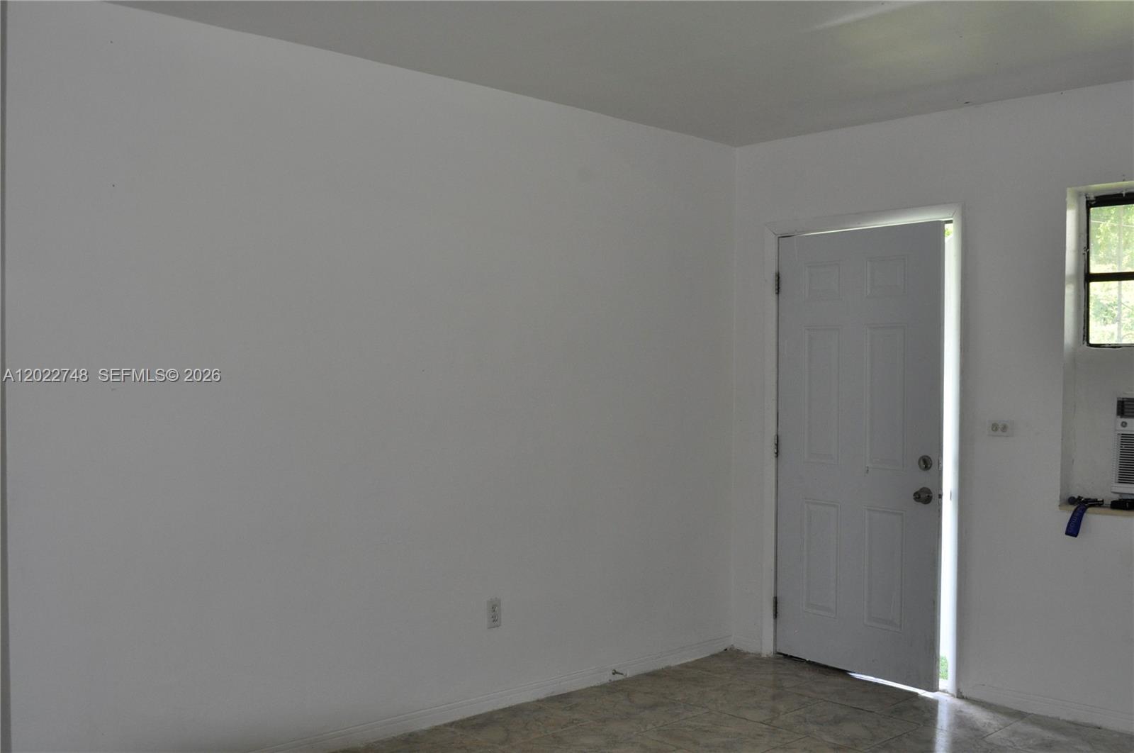 A sparsely furnished room features white walls, tile flooring, an open door, and a window — 2395 NW 82nd St # 2395, Miami FL 33147, MIAMI, FL