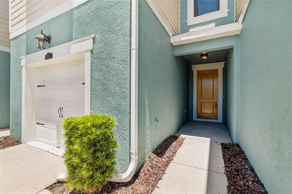 A teal stucco townhome exterior features a white garage door and a tan front door — 2410 ARCH AVENUE, OLDSMAR, FL