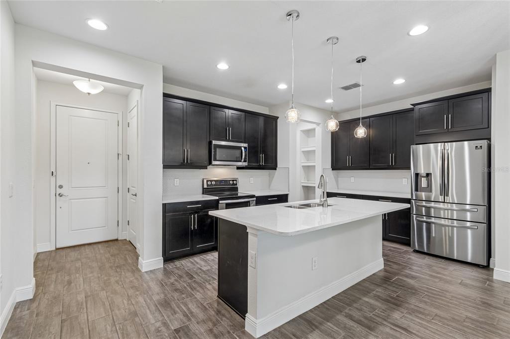 A modern kitchen features dark cabinetry, a white quartz island, and stainless steel appliances — 2410 ARCH AVENUE, OLDSMAR, FL