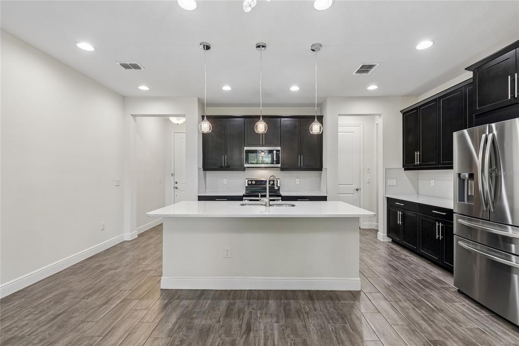 A modern kitchen features dark cabinets, a white quartz island, and wood-look tile flooring — 2410 ARCH AVENUE, OLDSMAR, FL