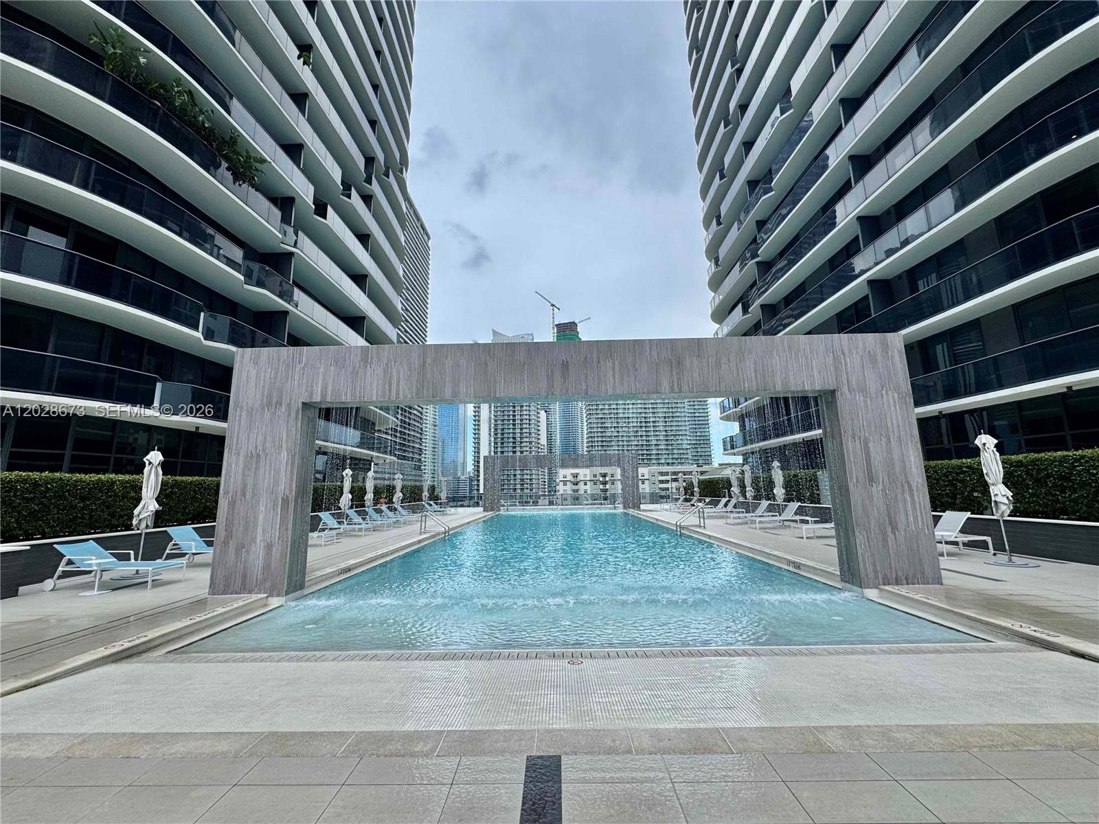 An outdoor swimming pool is framed by a stone archway between two modern high-rise buildings — 55 SW 9th St # 3201, Miami FL 33130, MIAMI, FL