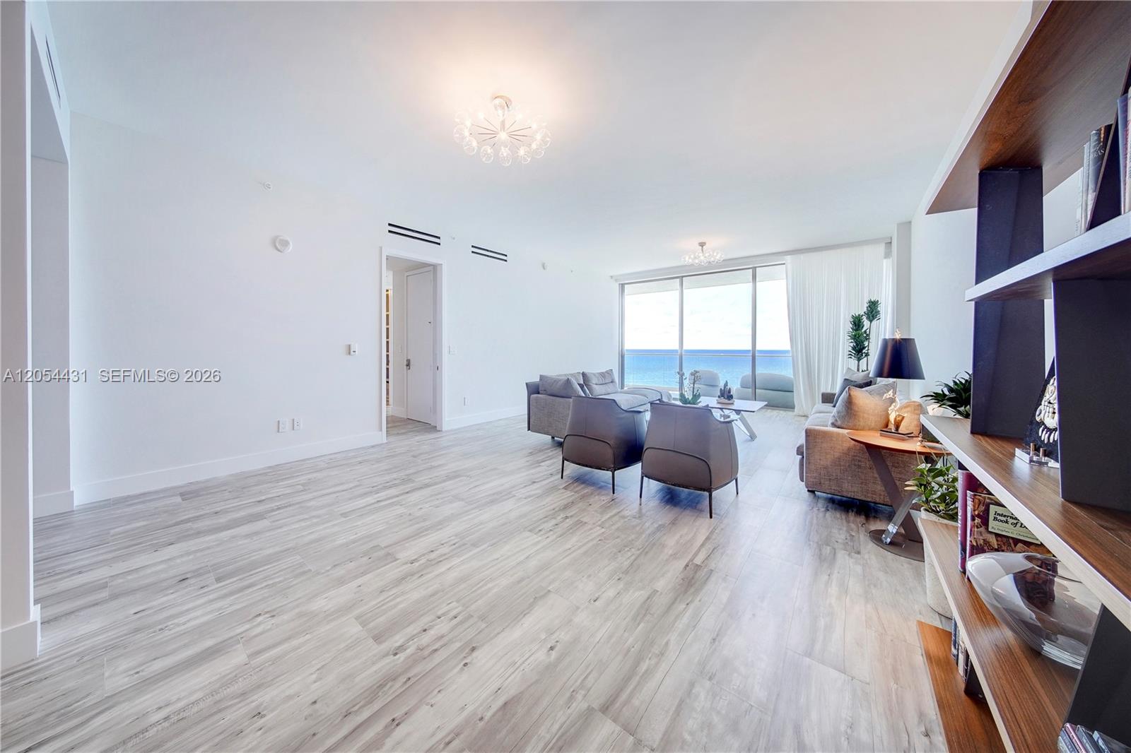 A bright living room features light wood-look flooring, modern furniture, and floor-to-ceiling ocean views — 10203 Collins Ave # 1502, Bal Harbour FL 33154, BAL HARBOUR, FL