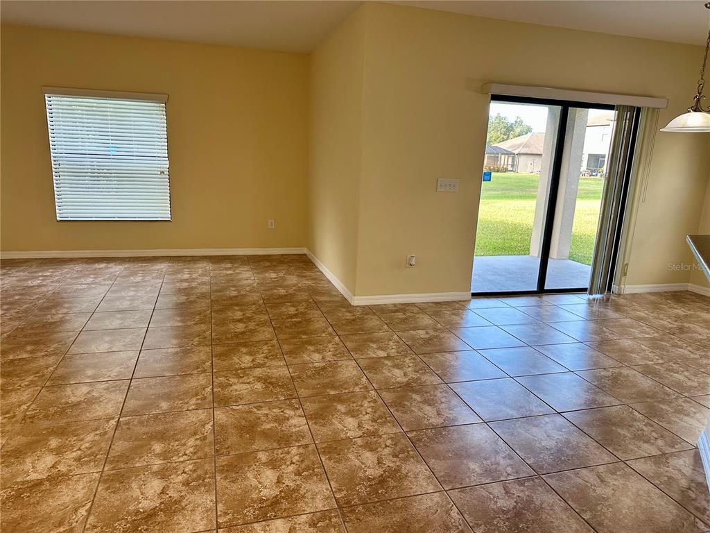 An open-concept room features light-colored walls, large square floor tiles, and a sliding glass door — 9908 SPICE BUSH COURT, TAMPA, FL