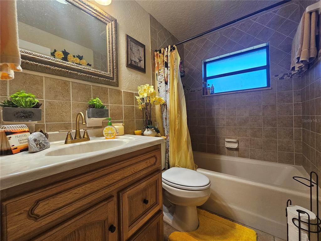 A bathroom features a wood vanity, a tiled tub-shower combination, and a yellow shower curtain — 3300 JAMES STREET, MELBOURNE, FL
