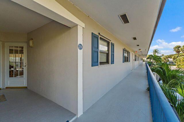 An exterior walkway with a blue railing overlooks palm trees outside a building with unit 206 — 755 Saturn Street # H207, Jupiter FL 33477, JUPITER, FL