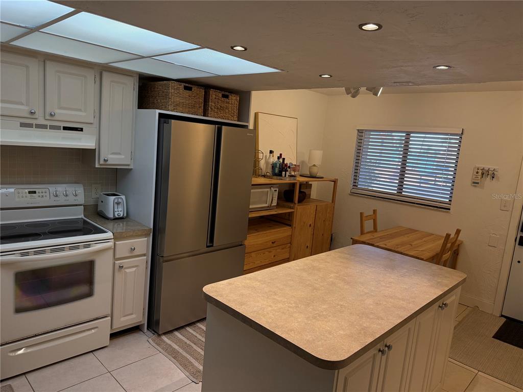 A kitchen features white cabinets, stainless steel appliances, a center island, and a dining area — 106 1ST STREET E UNIT 210, TIERRA VERDE, FL