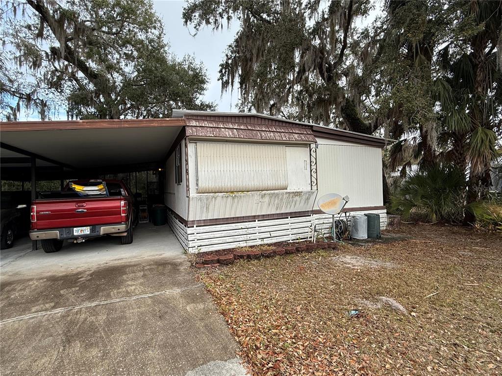 A single-story mobile home with a carport, a red pickup truck, and surrounding trees — 69 ROSALIE OAKS BOULEVARD, LAKE WALES, FL