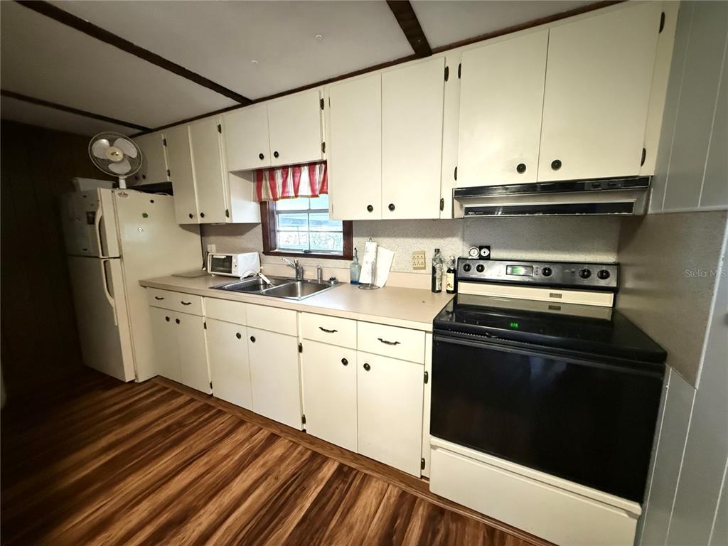 A kitchen features white cabinets, a black stove, a double sink, and wood-look flooring — 69 ROSALIE OAKS BOULEVARD, LAKE WALES, FL