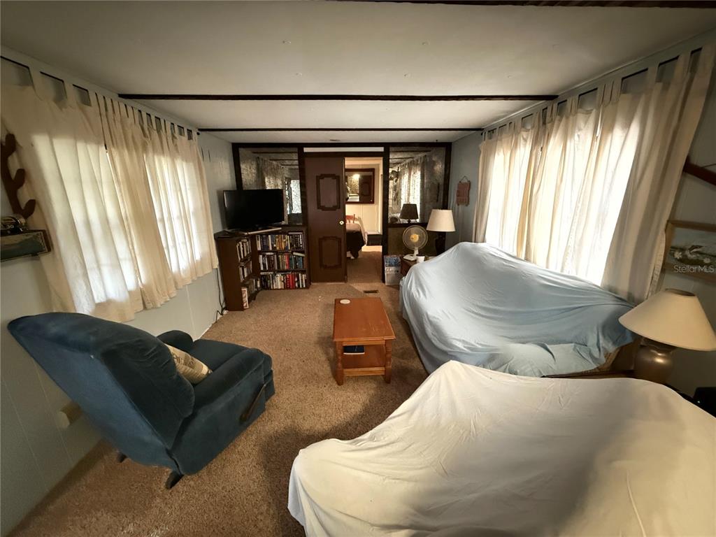 A living room with beige carpet, a blue armchair, and furniture covered in white sheets — 69 ROSALIE OAKS BOULEVARD, LAKE WALES, FL