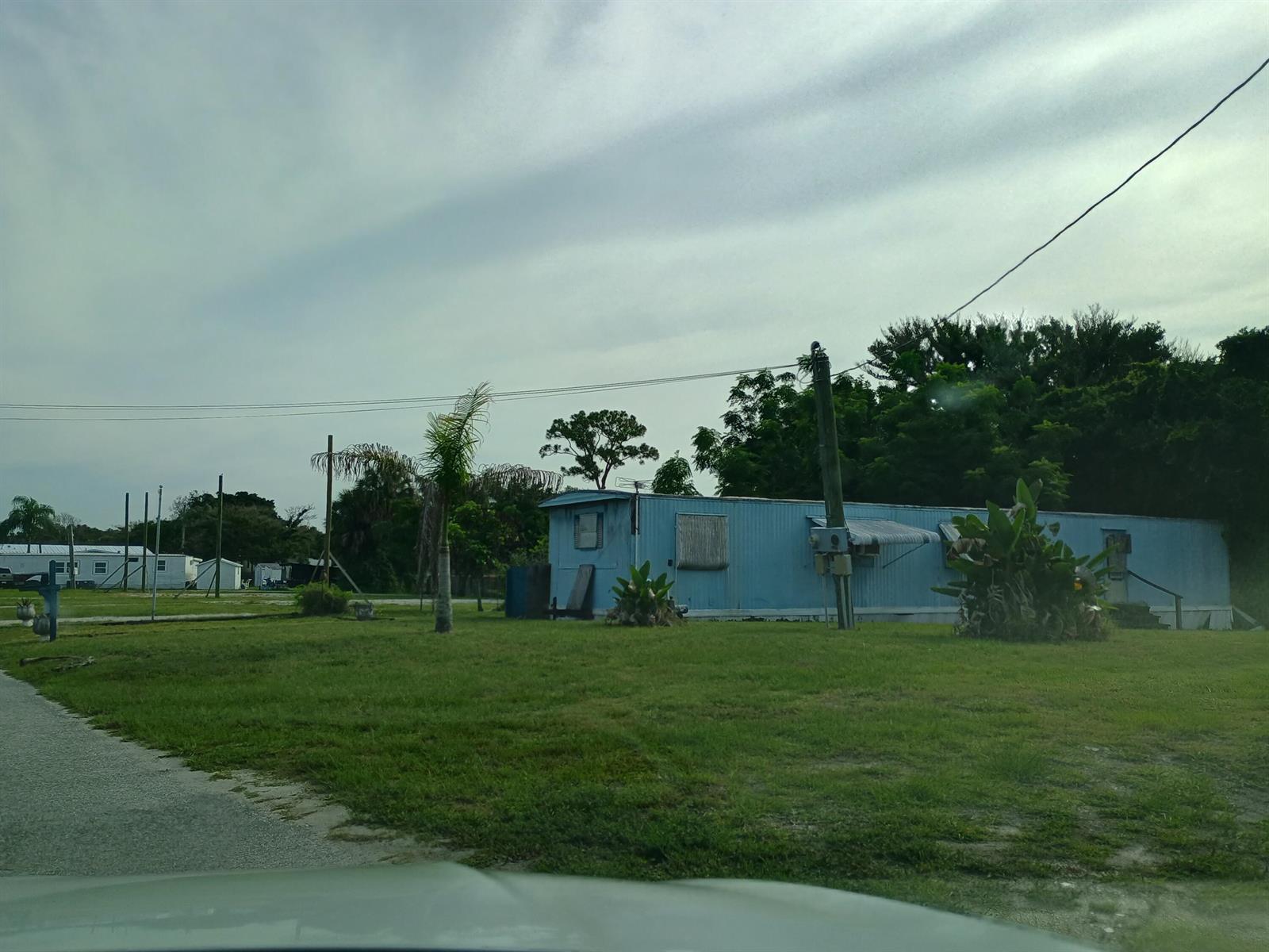 A blue mobile home sits on a grassy lot with a utility pole nearby — 1512 NE Dove Avenue, Stuart FL 34994, STUART, FL