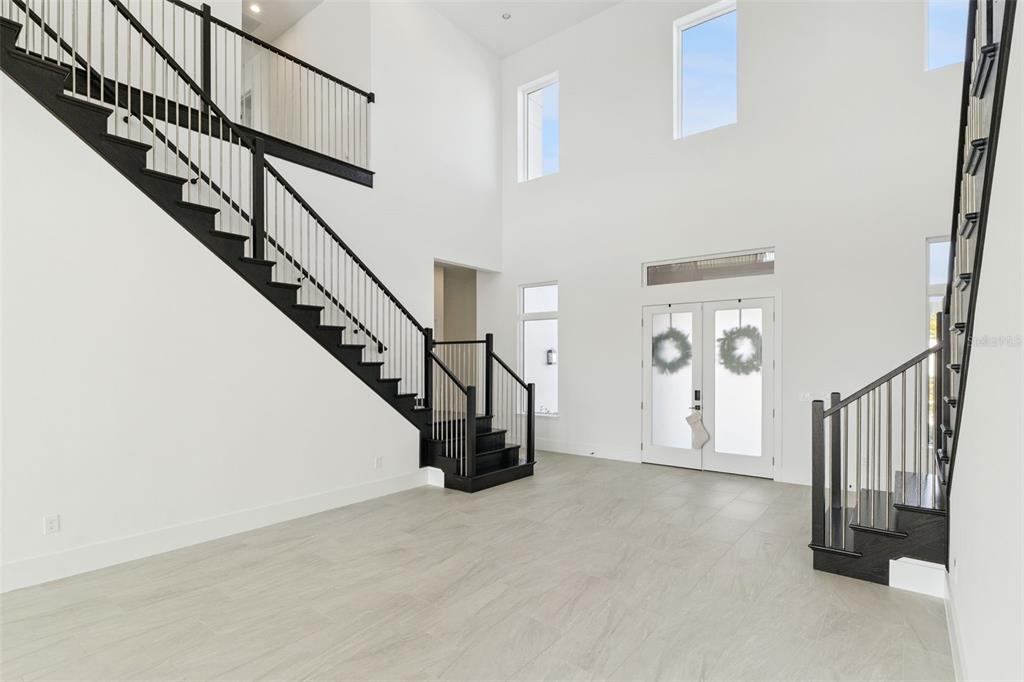 A bright, high-ceilinged foyer features light tile flooring and two black staircases with railings — 9720 LAUREL BERRY DRIVE, ORLANDO, FL
