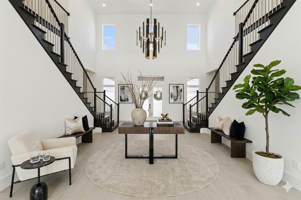 A grand foyer features dual staircases, a central console table, and a modern chandelier — 9720 LAUREL BERRY DRIVE, ORLANDO, FL