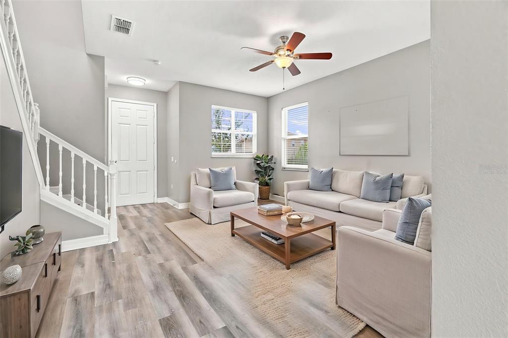 A living room features light gray walls, wood-look flooring, a staircase, and neutral-toned furniture — 4563 PHILADELPHIA CIRCLE, KISSIMMEE, FL