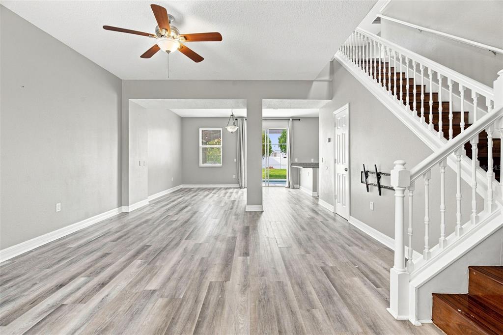An open living area features gray wood-look flooring, a ceiling fan, and a wooden staircase — 4563 PHILADELPHIA CIRCLE, KISSIMMEE, FL