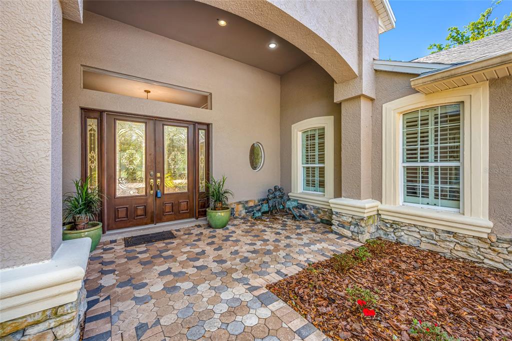 A front entryway features double glass doors, stone accents, and a patterned paver porch — 11939 PASCO TRAILS BOULEVARD, SPRING HILL, FL