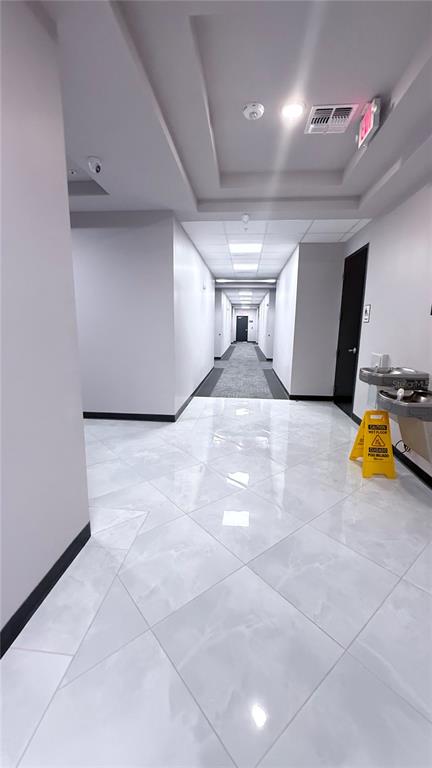 A hallway features white tiled floors, a recessed ceiling, and a water fountain with signage — 13564 VILLAGE PARK DRIVE UNIT 375, ORLANDO, FL