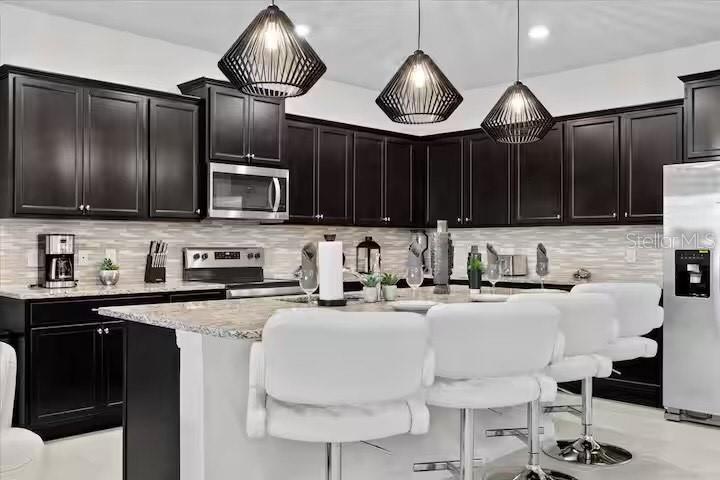 A modern kitchen features dark cabinetry, a central island with white stools, and pendant lighting — 2190 LELANI CIRCLE, DAVENPORT, FL