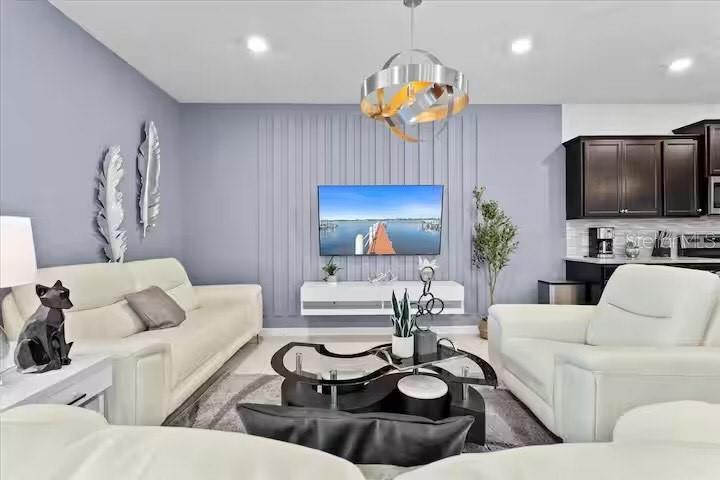 A living room with white sofas, a television on a paneled wall, and a chandelier — 2190 LELANI CIRCLE, DAVENPORT, FL