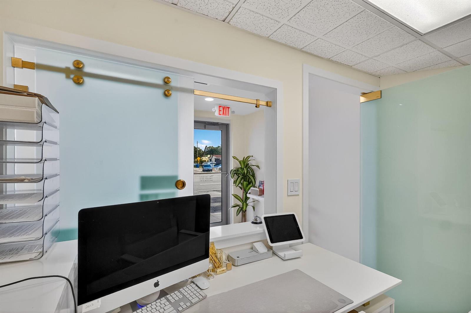 A reception desk with a computer and tablet sits before a frosted glass sliding window — Null Null Avenue, Miami FL 33145, MIAMI, FL