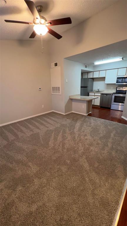 A carpeted living room opens into a kitchen with stainless steel appliances and wood flooring — 2206 ANTIGUA PLACE UNIT 1037, KISSIMMEE, FL