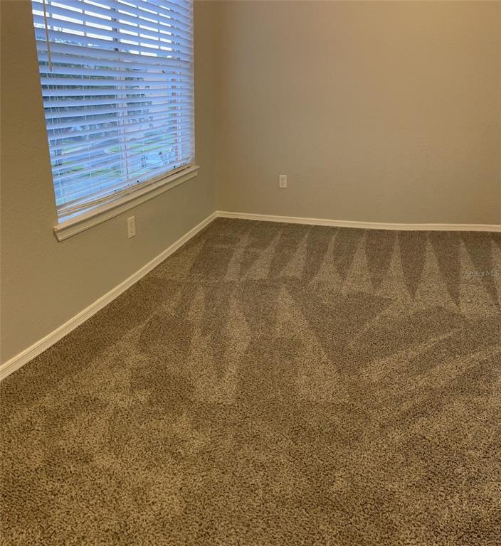 An empty bedroom features neutral walls, carpeted flooring, and a window with white blinds — 2206 ANTIGUA PLACE UNIT 1037, KISSIMMEE, FL