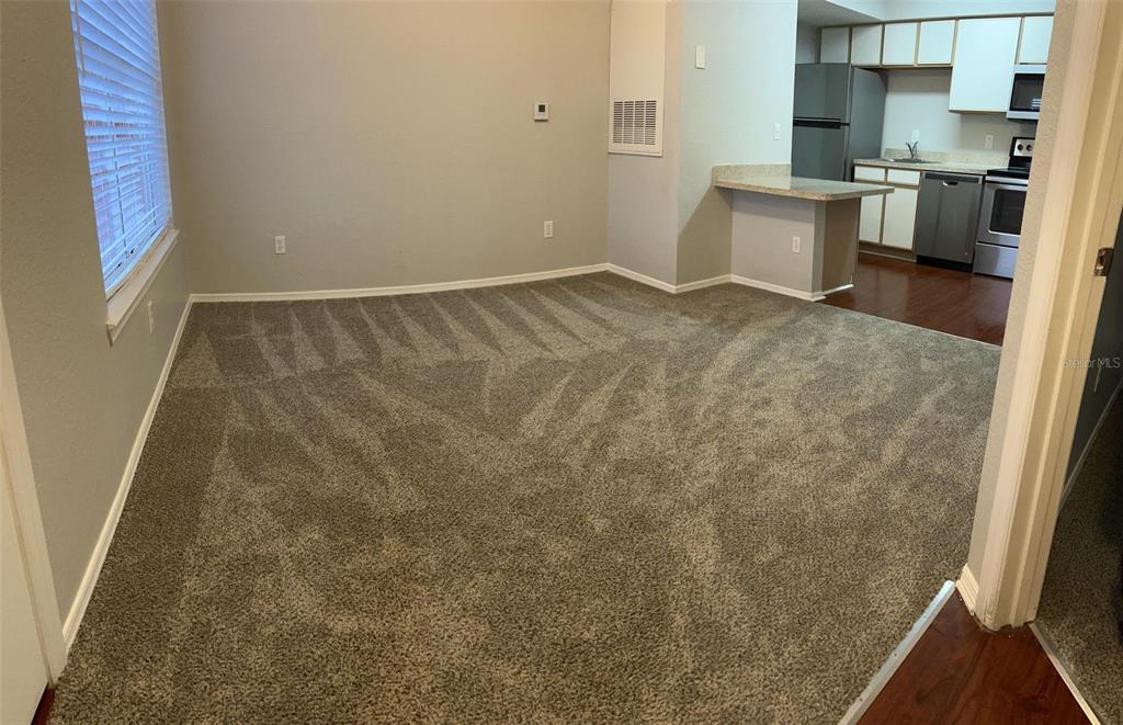A carpeted living area opens into a kitchen with stainless steel appliances and wood flooring — 2206 ANTIGUA PLACE UNIT 1037, KISSIMMEE, FL