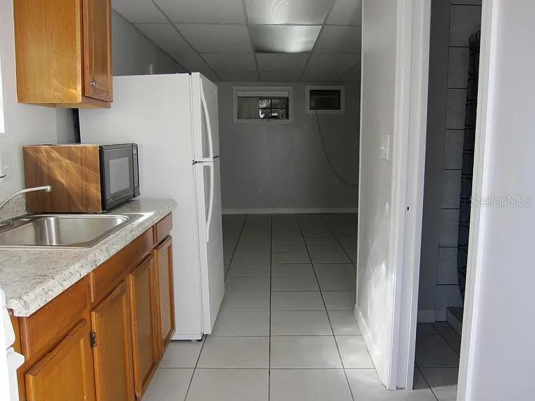 A kitchen with wood cabinets and a white refrigerator leads into a tiled living area — 28 N GROSSE AVENUE UNIT C, TARPON SPRINGS, FL