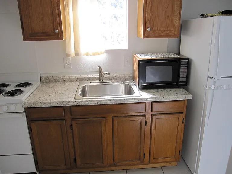 A kitchen features wood cabinets, a stainless steel sink, a microwave, and a white refrigerator — 28 N GROSSE AVENUE UNIT C, TARPON SPRINGS, FL