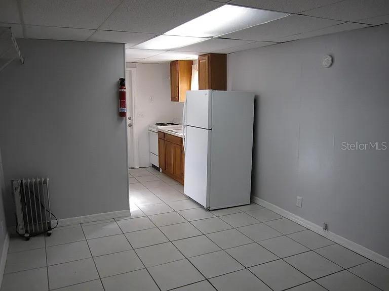 A kitchen with wood cabinets and a white refrigerator sits adjacent to a tiled room — 28 N GROSSE AVENUE UNIT C, TARPON SPRINGS, FL