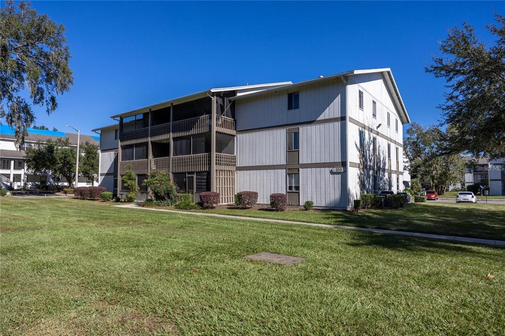 A three-story apartment building with light-colored siding and screened-in balconies stands on a grassy lawn — 6519 W NEWBERRY ROAD UNIT 108, GAINESVILLE, FL