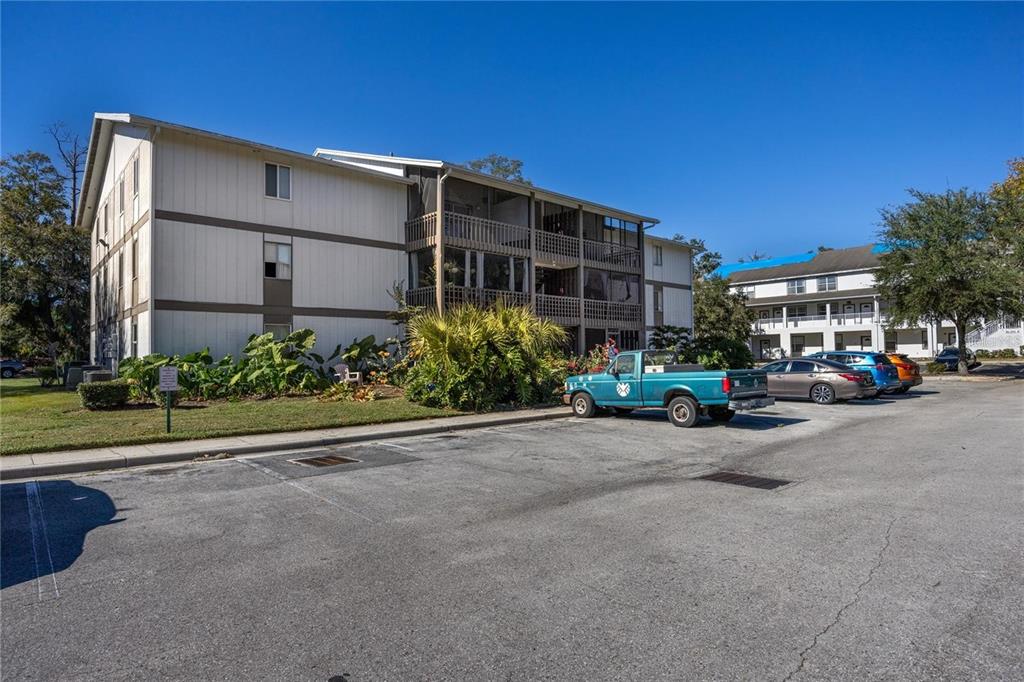 A three-story apartment building with screened balconies sits behind a parking lot with several cars — 6519 W NEWBERRY ROAD UNIT 108, GAINESVILLE, FL