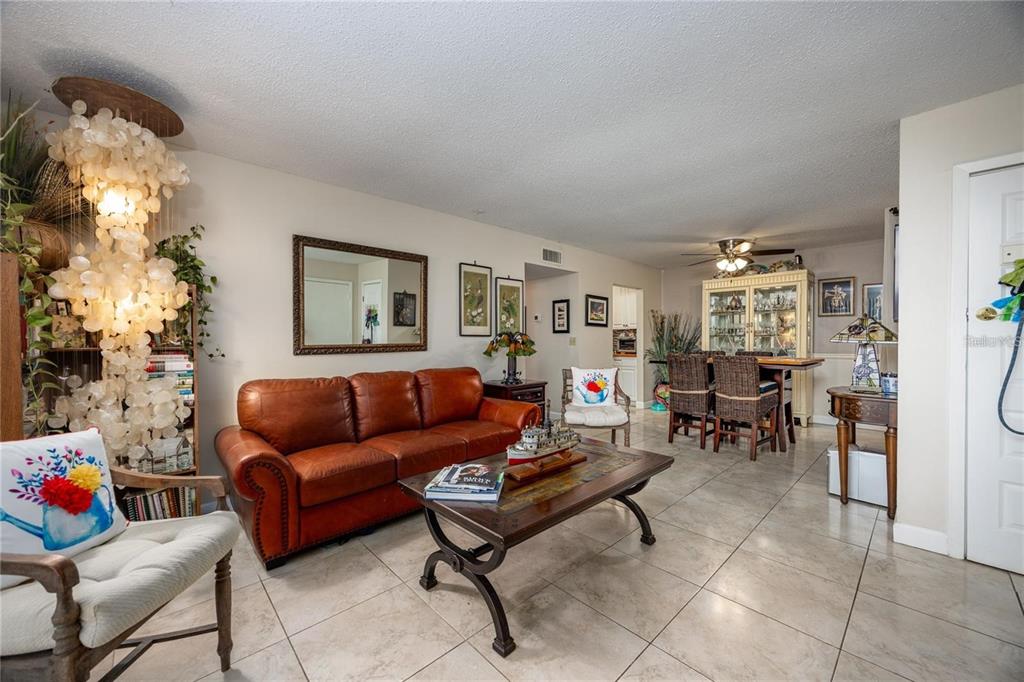 A living room with a leather sofa, tile flooring, and a large decorative light fixture — 6519 W NEWBERRY ROAD UNIT 108, GAINESVILLE, FL