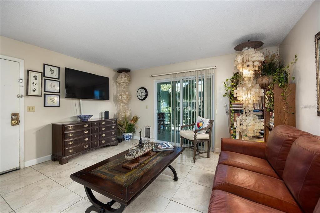 A living room features tile flooring, a leather sofa, a wooden coffee table, and shell chandeliers — 6519 W NEWBERRY ROAD UNIT 108, GAINESVILLE, FL