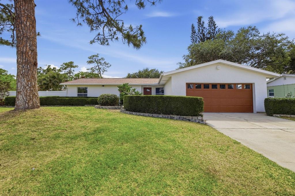 A single-story white house with a brown garage door and a manicured hedge in front — 7520 20TH STREET N, ST PETERSBURG, FL