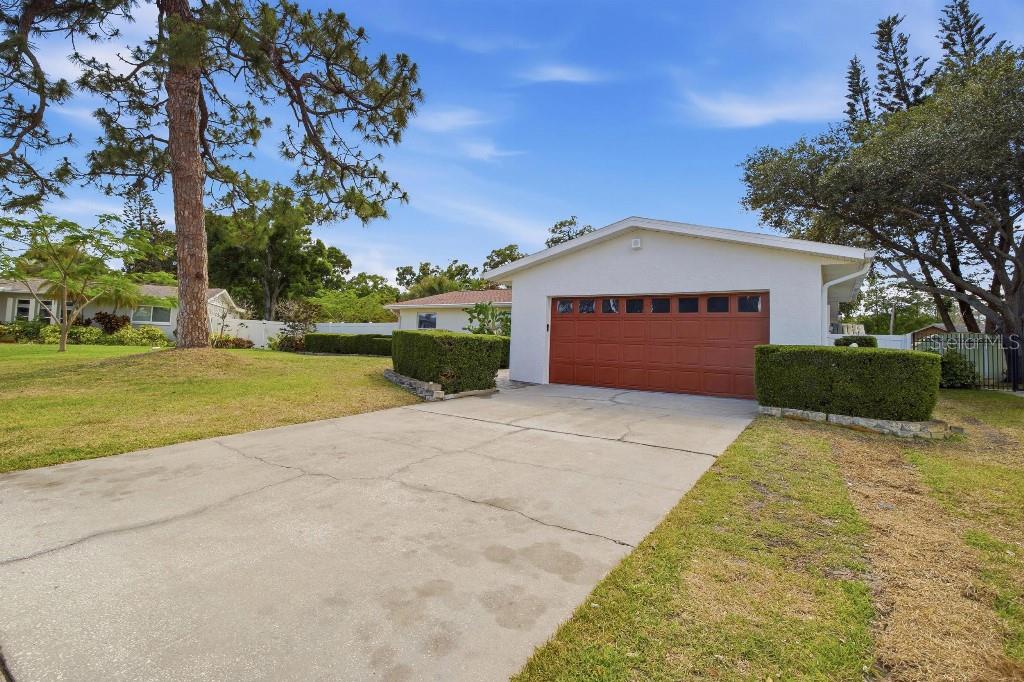 A concrete driveway leads to a white house with a brown two-car garage door — 7520 20TH STREET N, ST PETERSBURG, FL