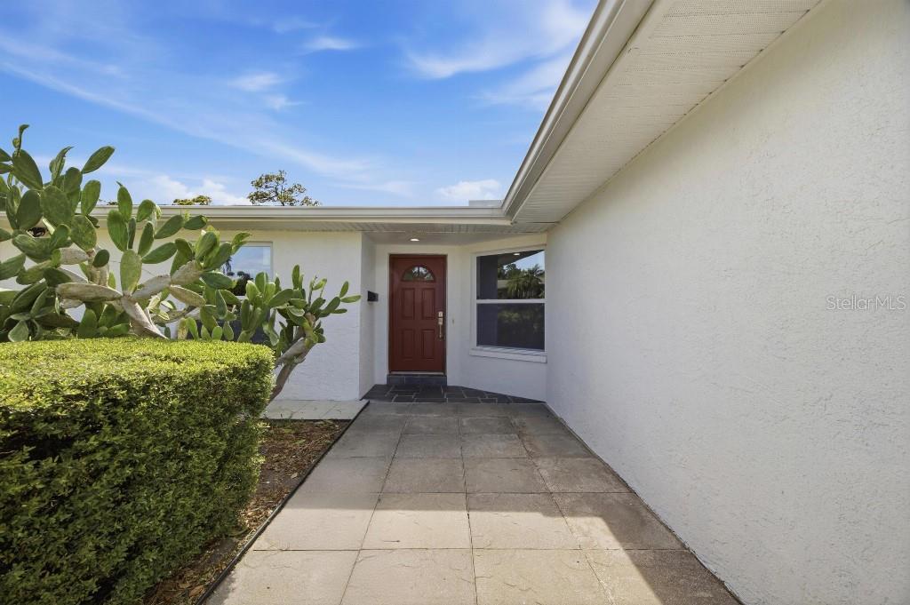 A paved walkway leads to a red front door of a white house with cacti — 7520 20TH STREET N, ST PETERSBURG, FL