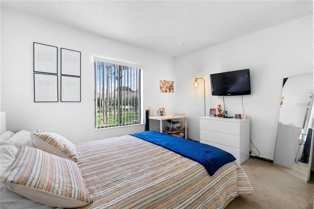 A bedroom features a bed with striped bedding, a desk, a dresser with a television, and a window — 8217 SUN SPRING CIRCLE UNIT 72, ORLANDO, FL