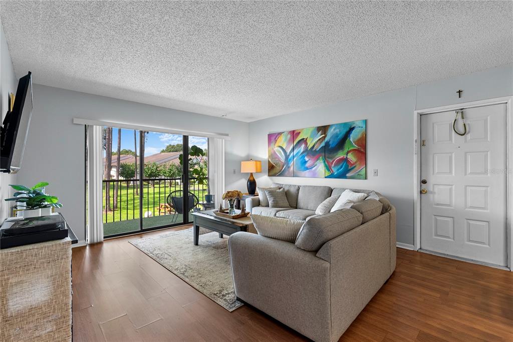 A living room features wood-look flooring, a gray sectional sofa, and a sliding glass door — 8217 SUN SPRING CIRCLE UNIT 72, ORLANDO, FL