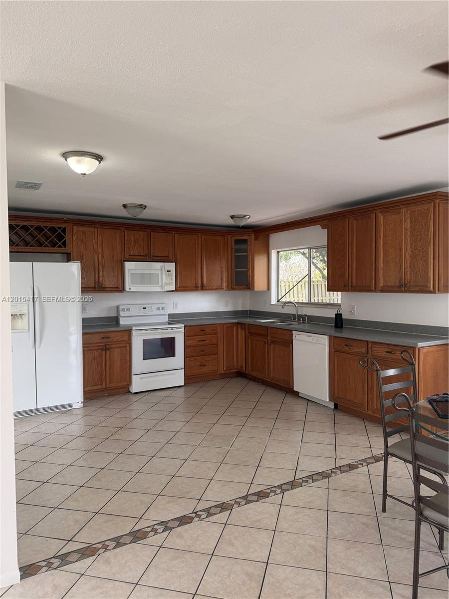 A kitchen features wood cabinets, white appliances, gray countertops, and light-colored tile flooring — 731 SW 24th St, Vero Beach FL 32962, VERO BEACH, FL